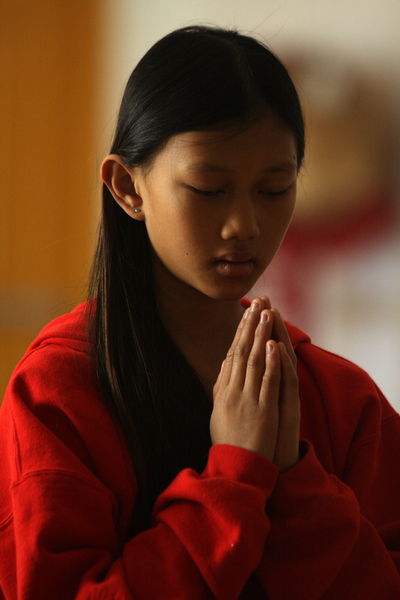 11-year-old Emily Morgan Tracey at prayer during services. About her experiences as a Vietnamese American, she says, "It can be hard to be Asian and American because sometimes people tease you. But believe in who you are and dont let anyone or anything stop you."